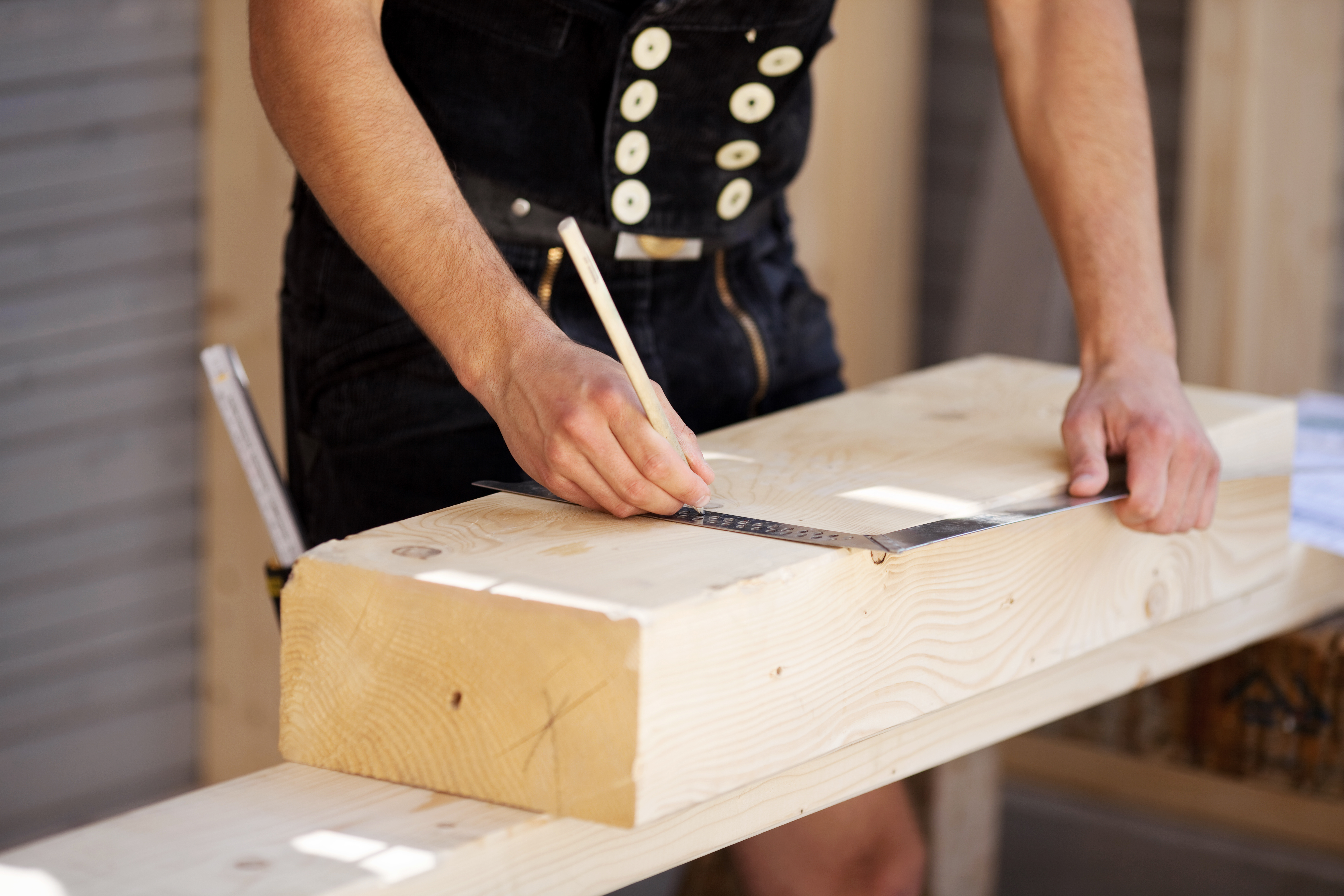 Handwerker misst Holzblock aus und markiert Stellen